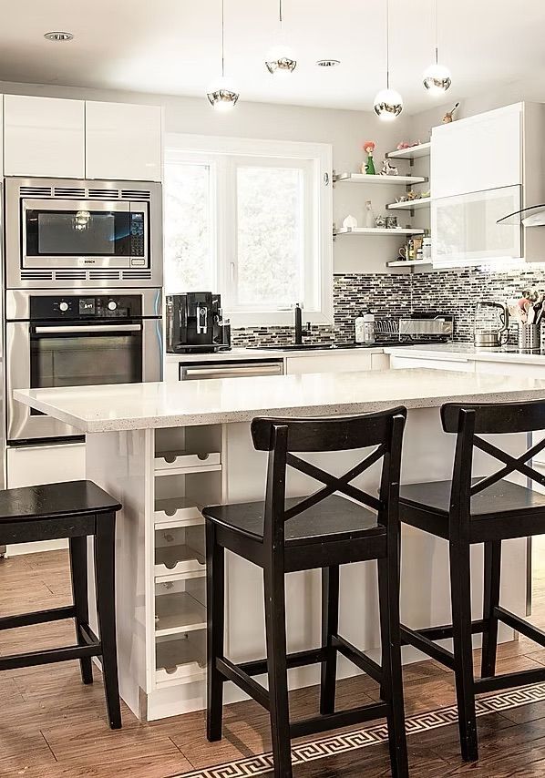 Cuisine moderne avec armoires blanches, îlot avec tabourets noirs et électroménagers en acier inoxydable.