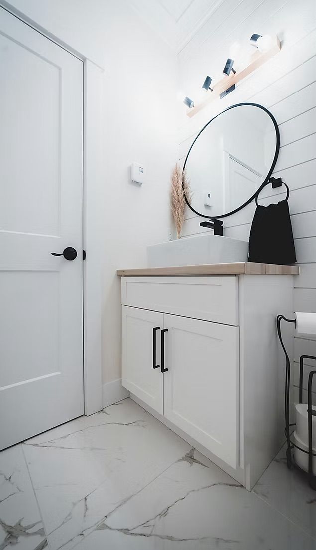 Salle de bain blanche avec une vanité, un miroir rond et une serviette noire.