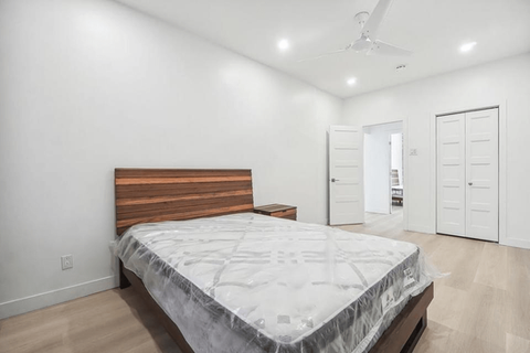 Chambre avec un cadre de lit marron, un matelas enveloppé et des murs et des portes blancs.
