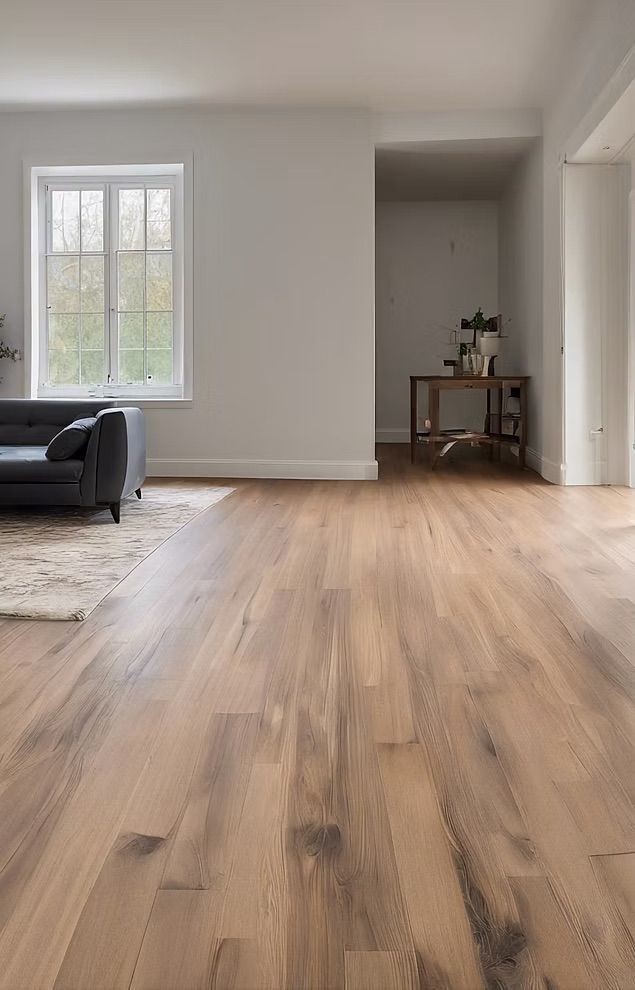 Salon avec parquet, un canapé sombre, une fenêtre et une table en arrière-plan.