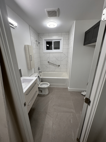 Une petite salle de bain moderne avec baignoire, toilettes et lavabo. Carrelage et sol blancs et gris.