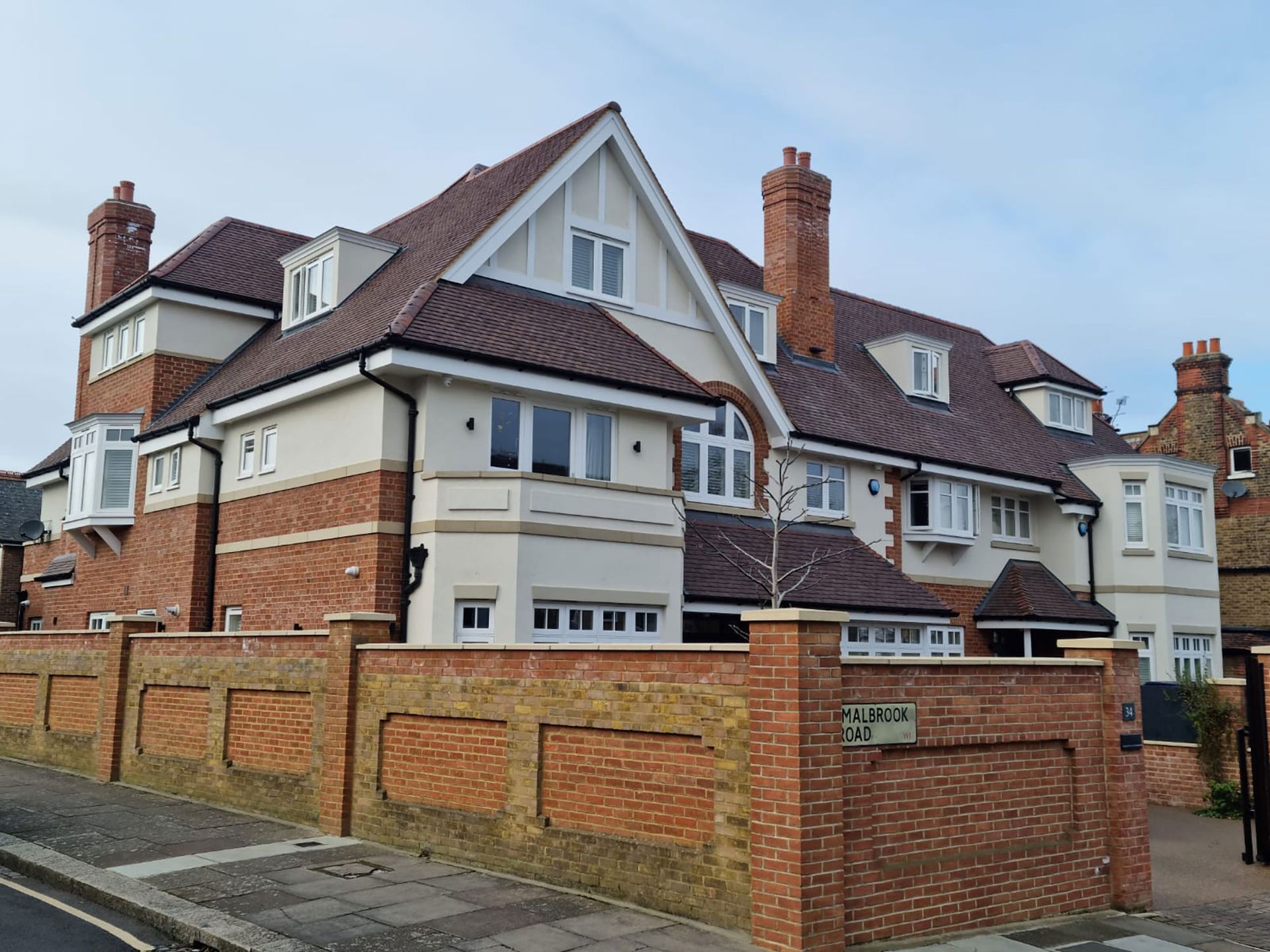 Large brick and stucco house with multiple rooflines, chimneys, and a low brick wall.