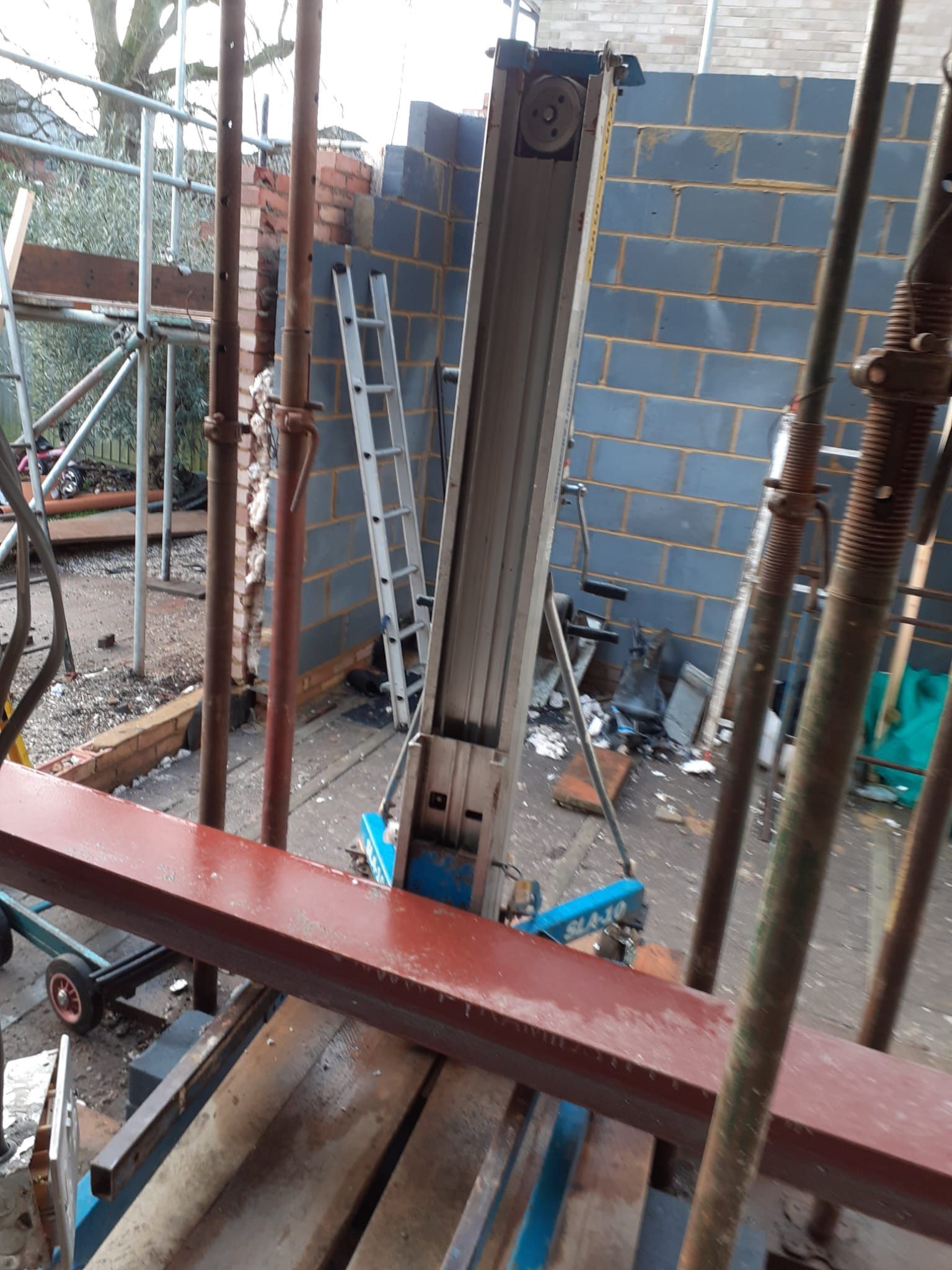 Construction site with scaffolding, a conveyor lift, cinder block wall, and ladder.