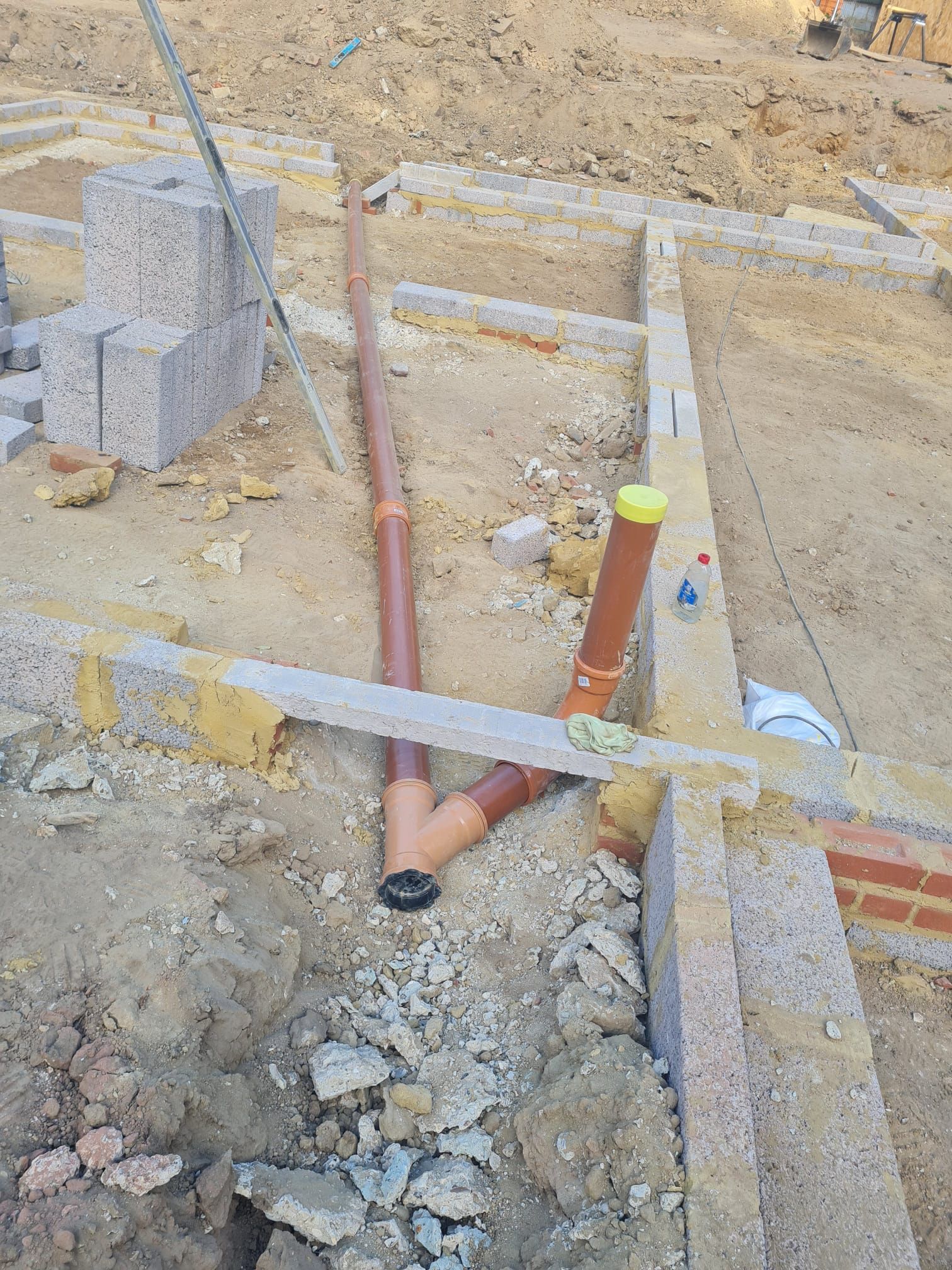 Construction site with brown drainage pipes laid in trenches, alongside concrete and brick structures.