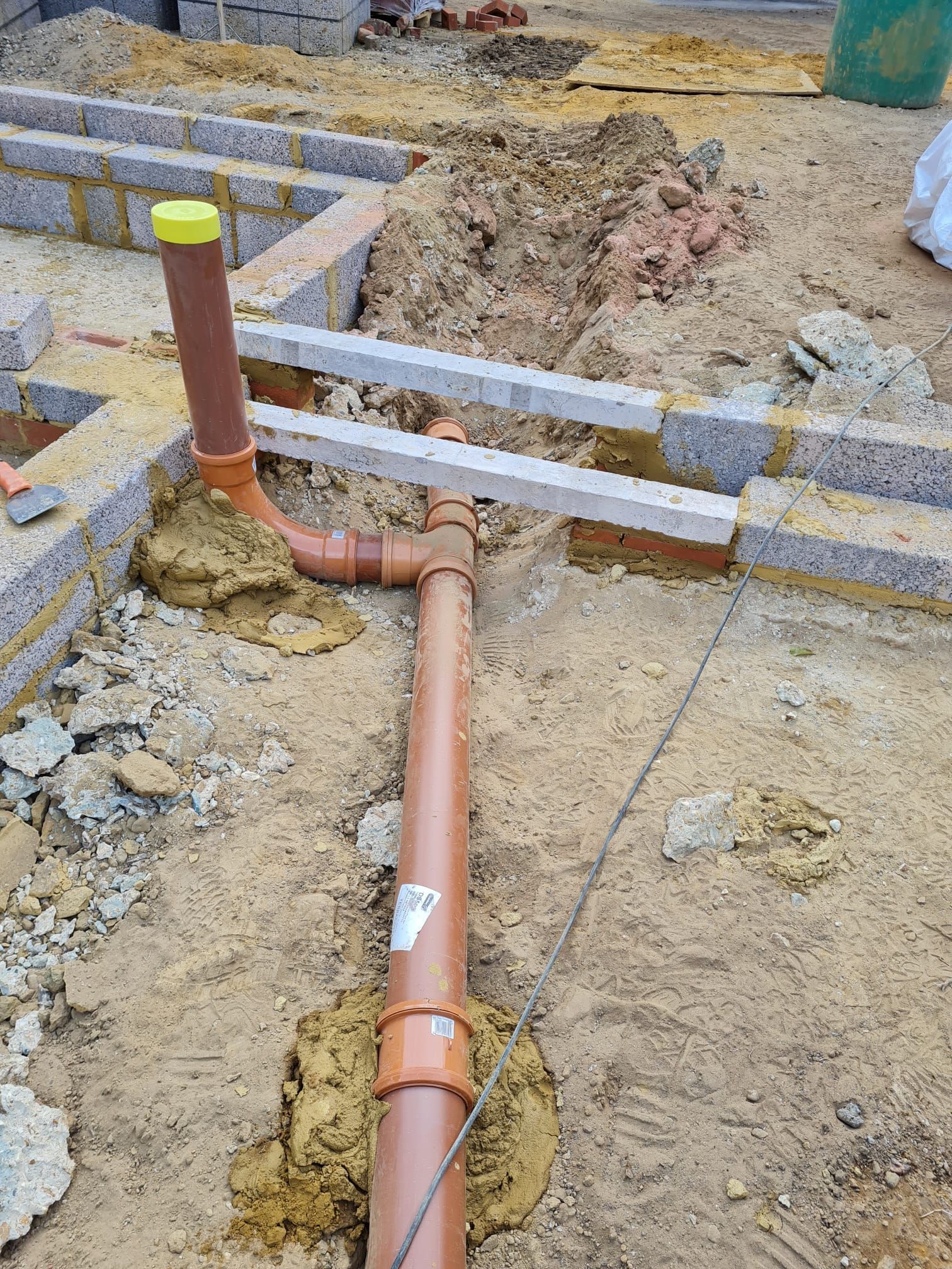 Orange PVC drainage pipes and connections amidst construction site dirt and concrete blocks.