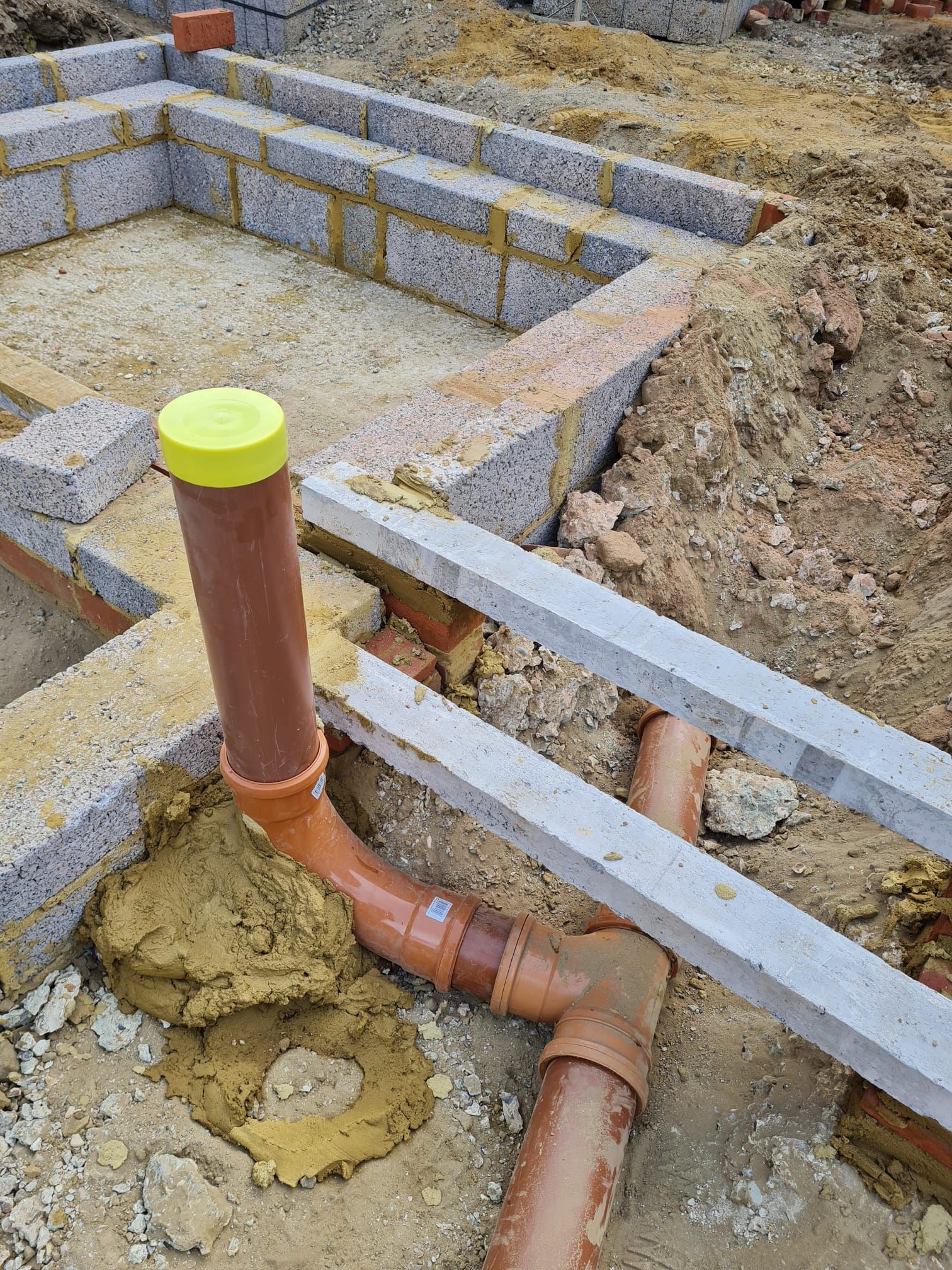 Construction site with brown drainage pipes, gray cinder block foundation, and yellow cap.