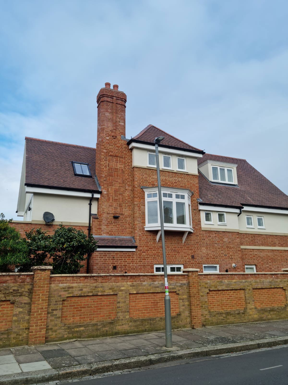 Brick house with red roof, tall chimney, white trim, and a brick wall along the street.