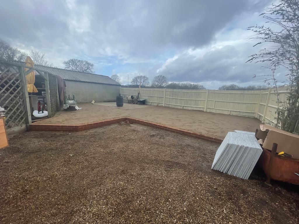 Gravel backyard with brick border, shed, fence, and stacked white panels. Cloudy sky.