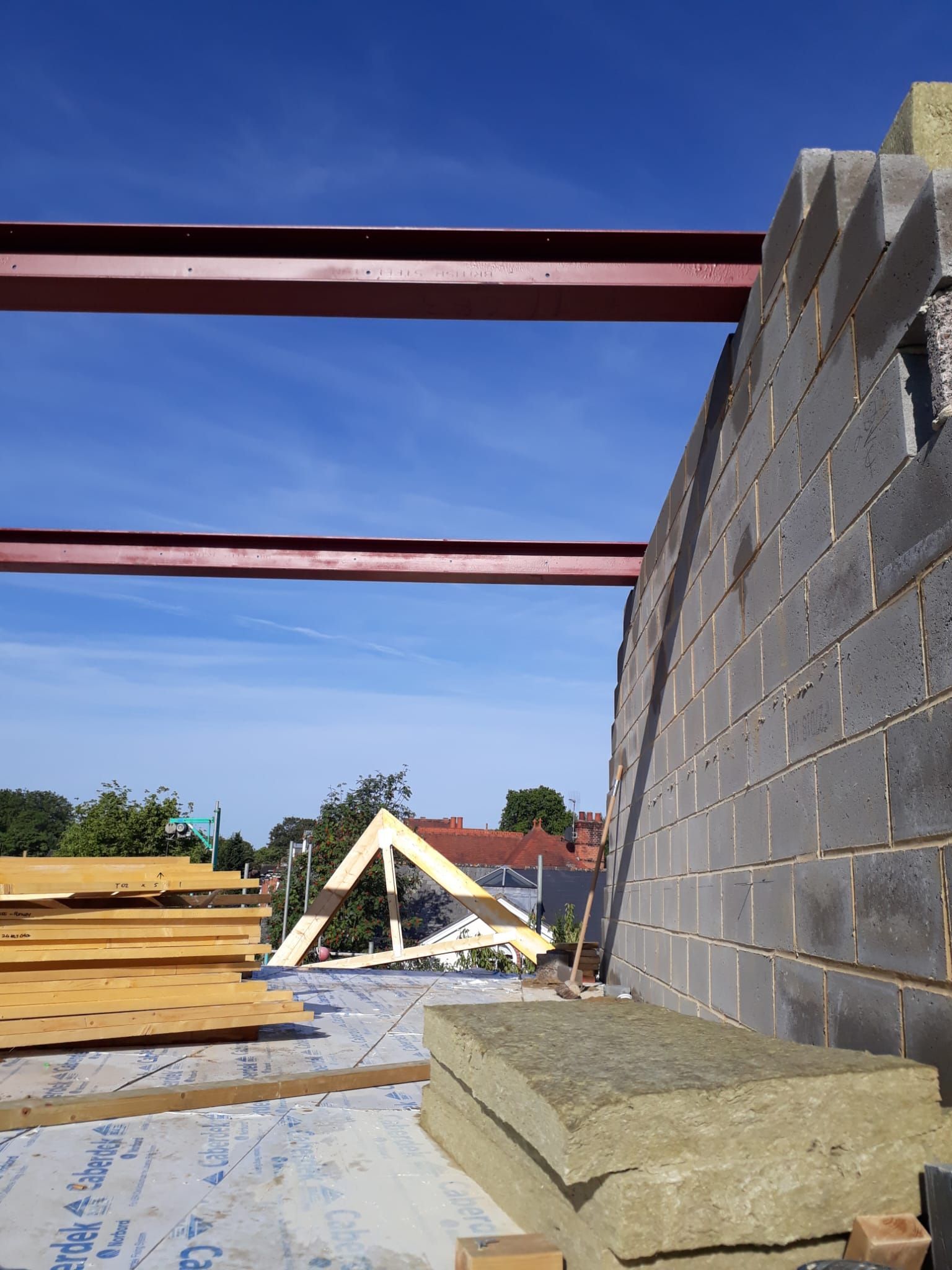 Construction site with brick wall, metal beams, wood, and insulation against a blue sky.
