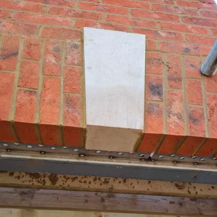 Beige stone block set into a red brick wall above a metal and wood structure.