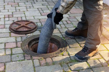 Person holding a hose, draining a manhole on a brick-paved surface.