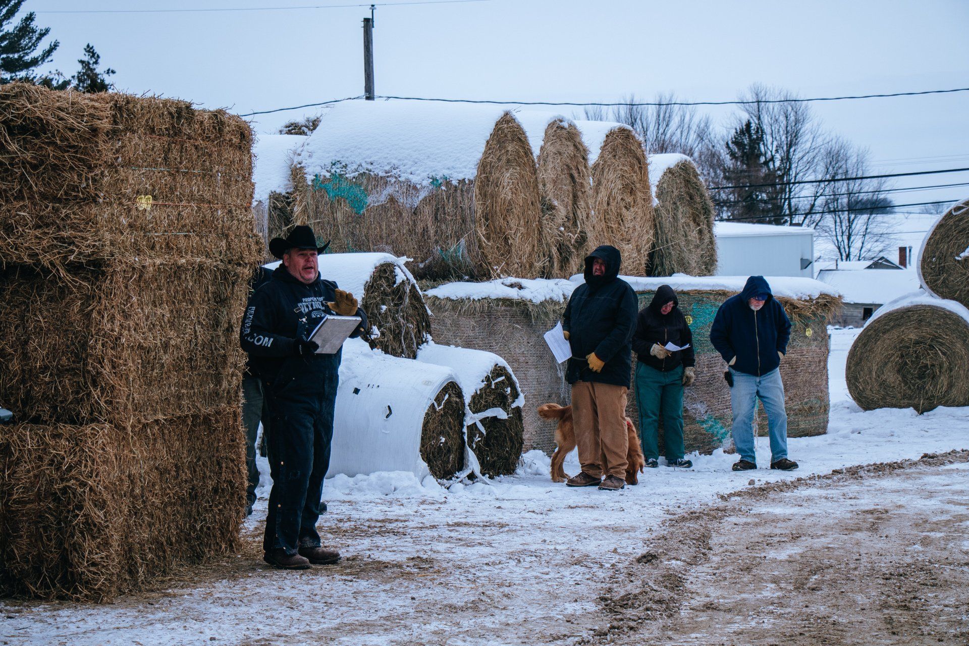 People standing near large hay bales in a snowy rural field during winter
