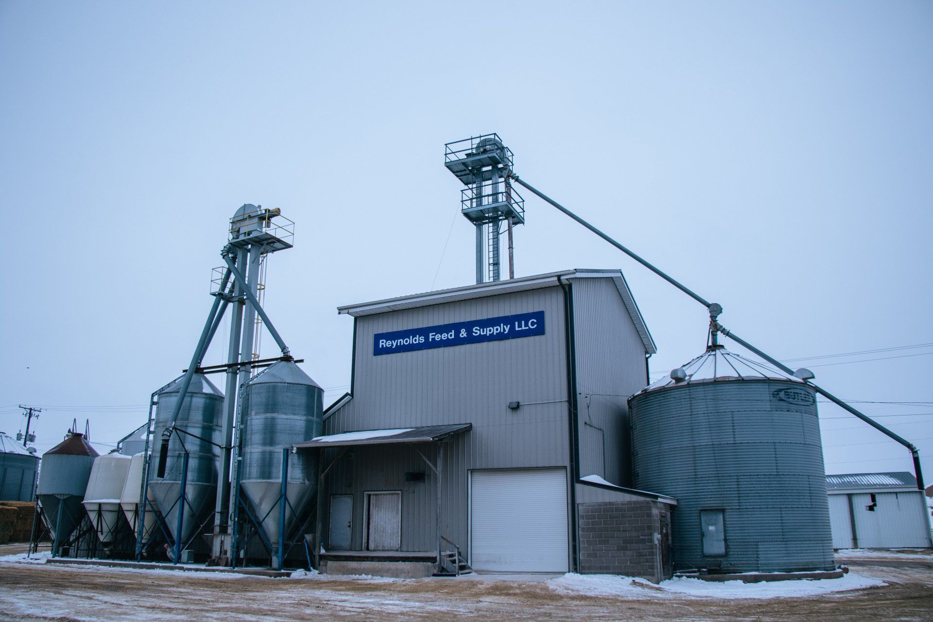 Snowy grain elevator and silos at a rural industrial site under an overcast sky