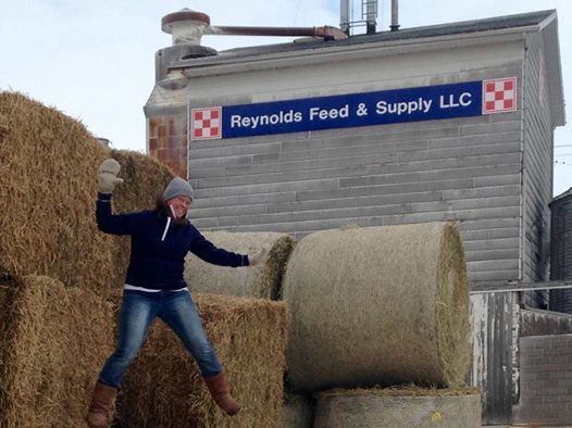 Person standing by stacked hay bales outside Reynolds Feed & Supply LLC building