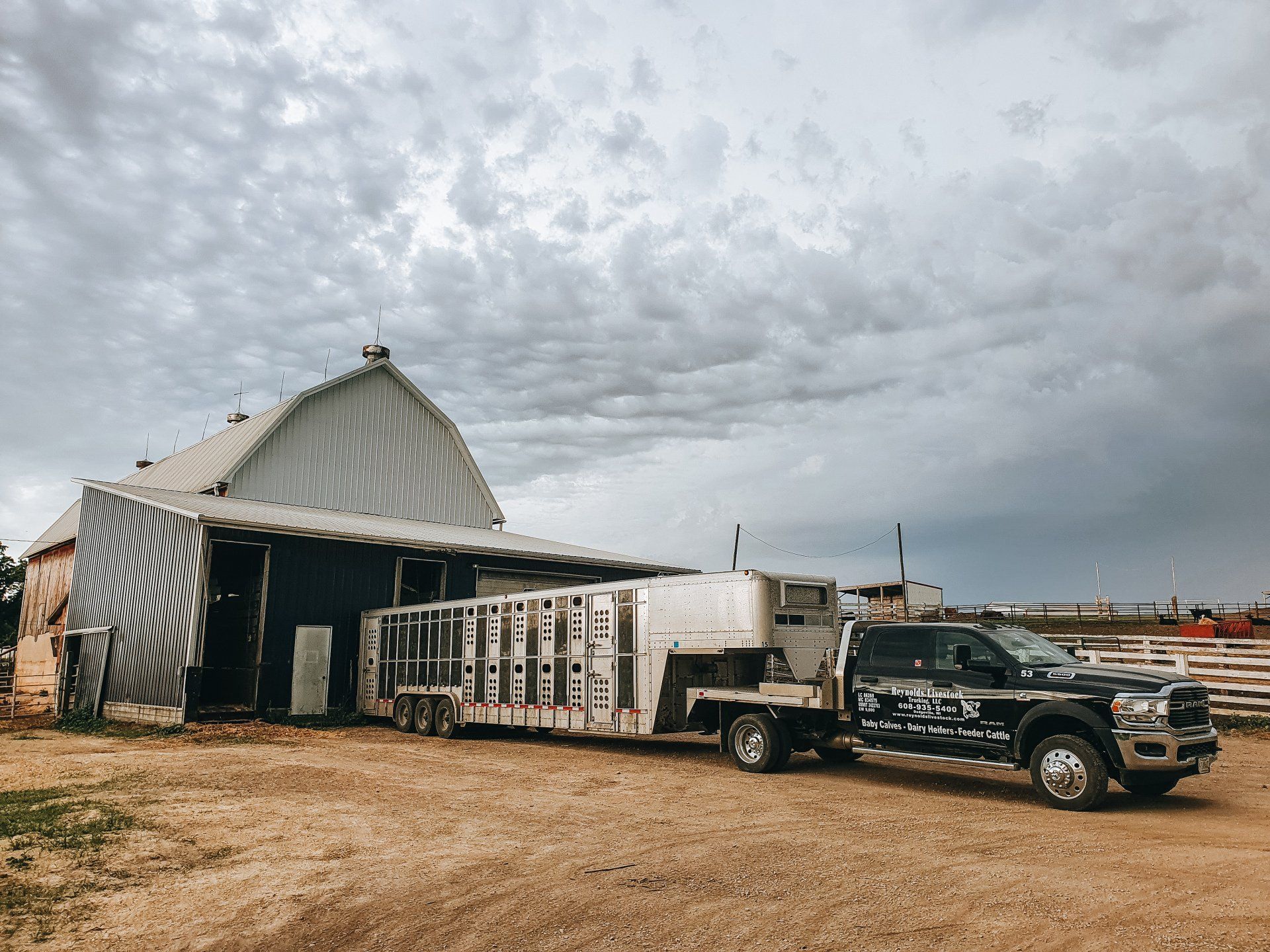 White truck and dark SUV beside a striped tent in a dry field under a cloudy sky