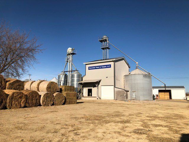 Farm grain silos and storage buildings beside hay bales under a clear blue sky