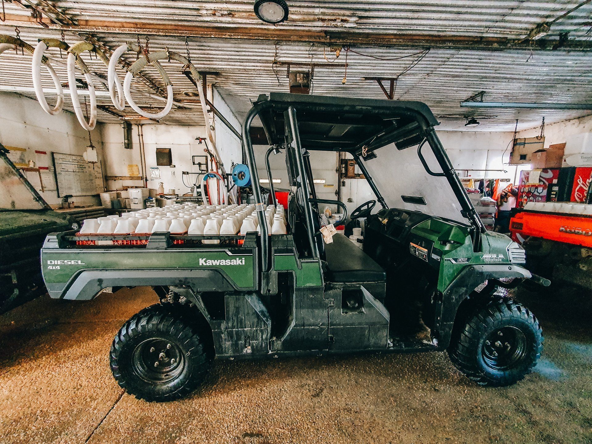 Green Kawasaki utility vehicle parked inside a workshop with tools and equipment in the background