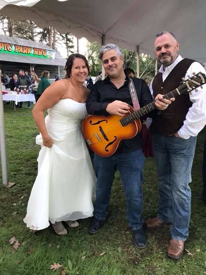 A bride and groom are posing for a picture with a man holding a guitar.