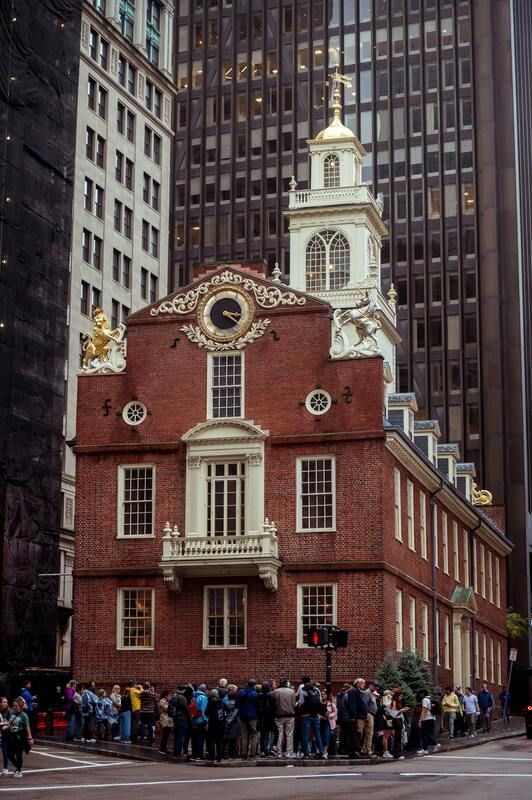 A group of people are standing in front of a brick building with a clock tower.