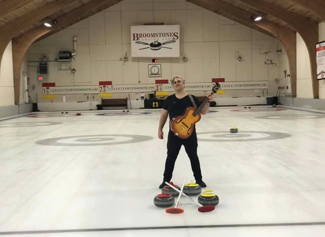 A man standing on a curling rink holding a guitar