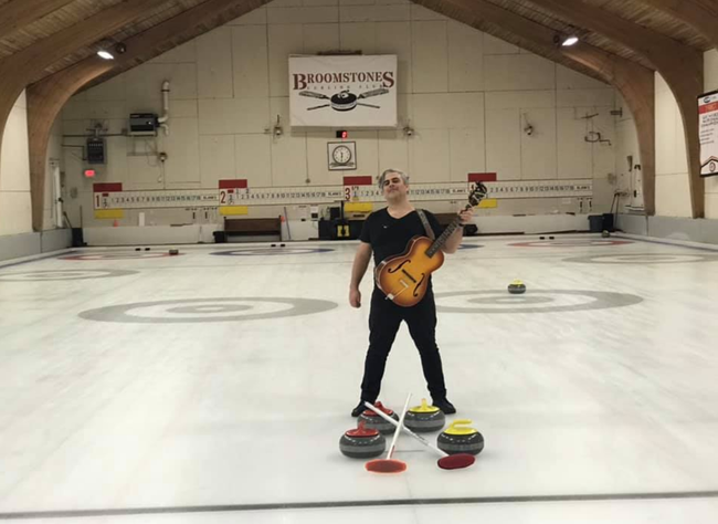 A man standing on a curling rink holding a guitar