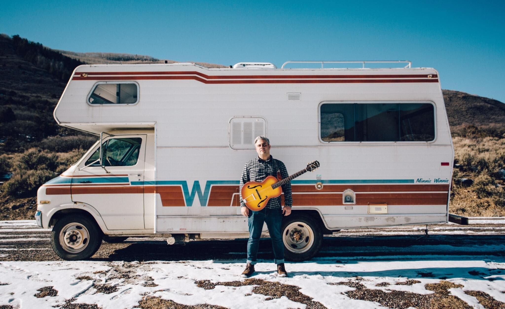 Person standing in front of a white camper van in a snowy mountain landscape