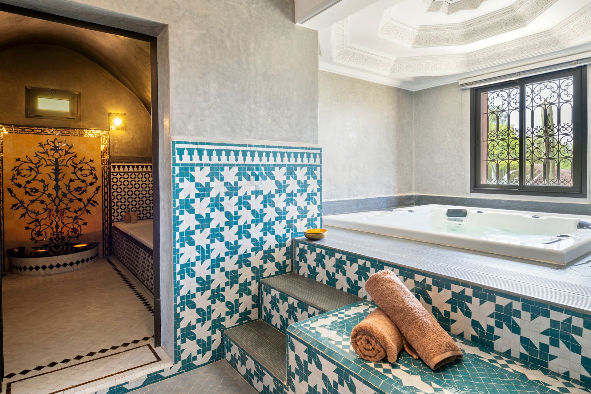 Tiled spa room with a sunken bathtub, turquoise benches, and an arched doorway to a sauna.