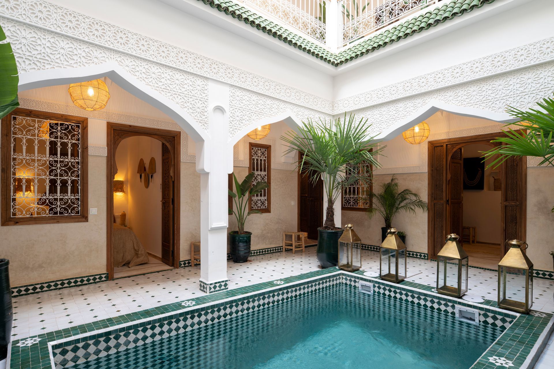 Elegant indoor courtyard with a tiled pool, white arches, potted palms, and warm wall lanterns