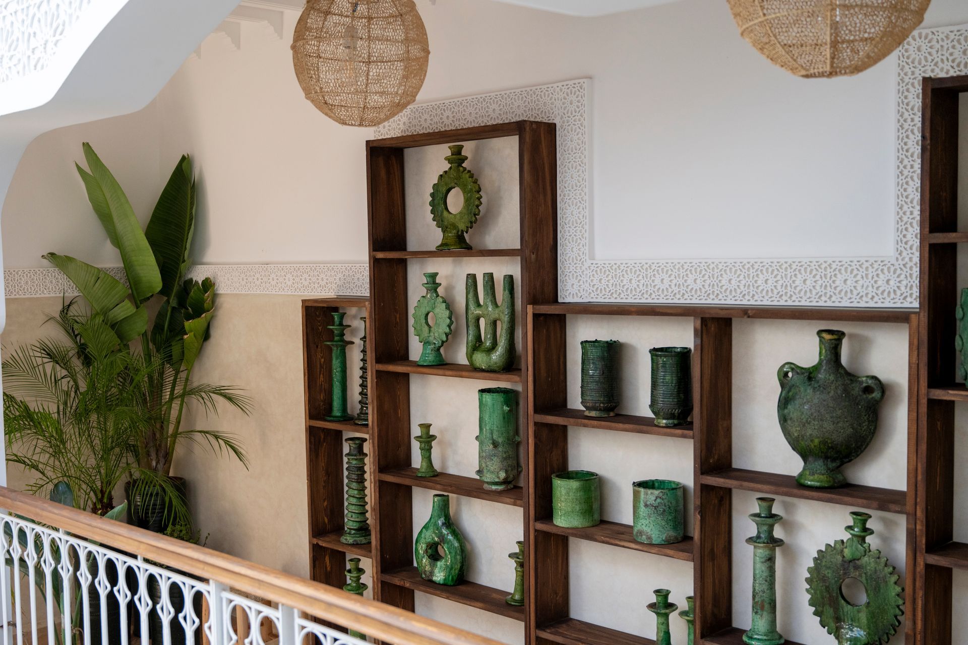 Green decorative pottery on wooden shelves in a bright interior with woven hanging lamps and plants