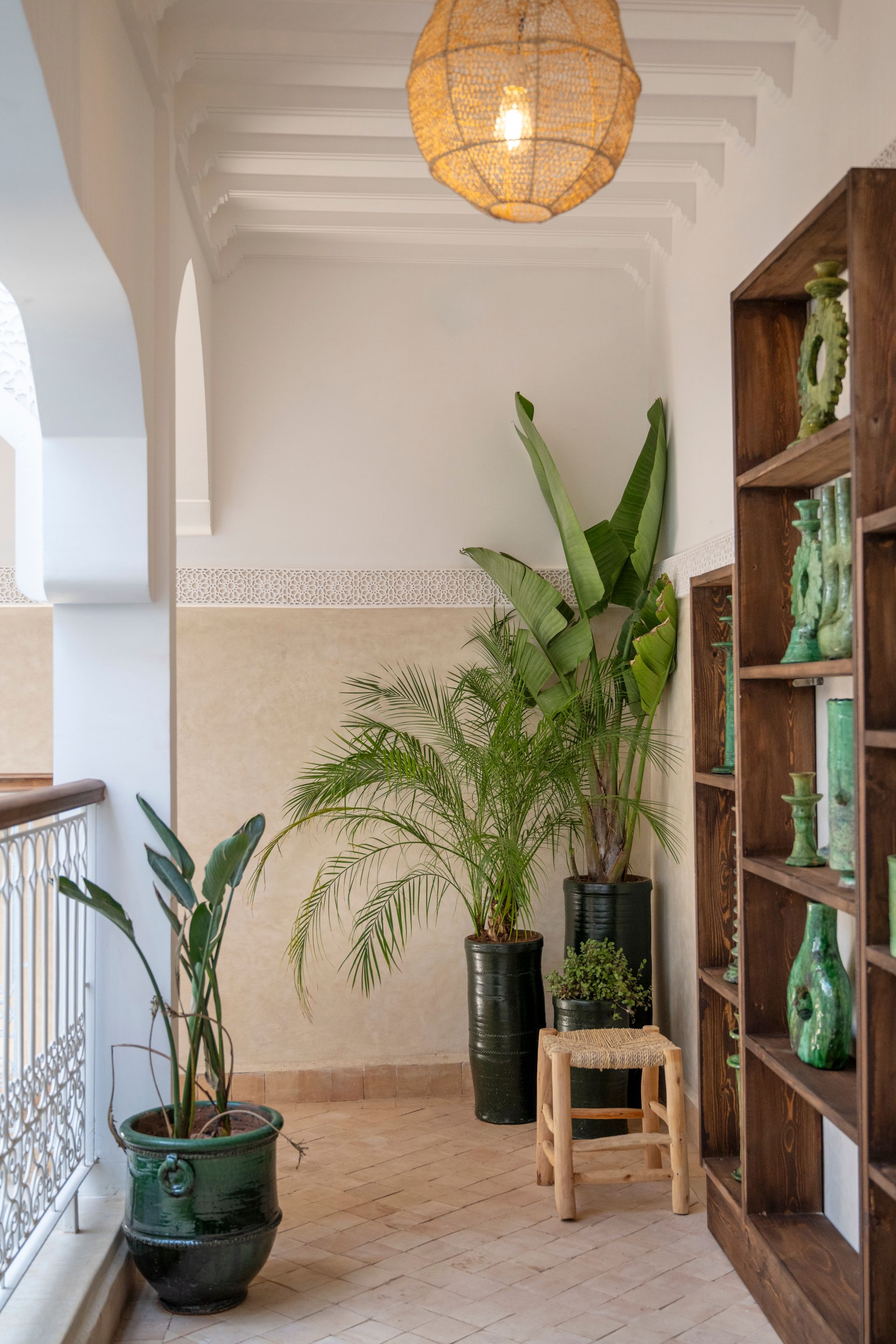Bright hallway with potted plants, a hanging woven lamp, and a wooden shelf against white walls.