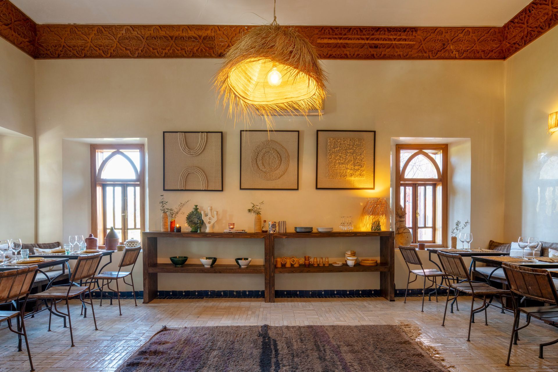 Cozy dining room with wooden tables, arched windows, framed art, and a woven pendant light