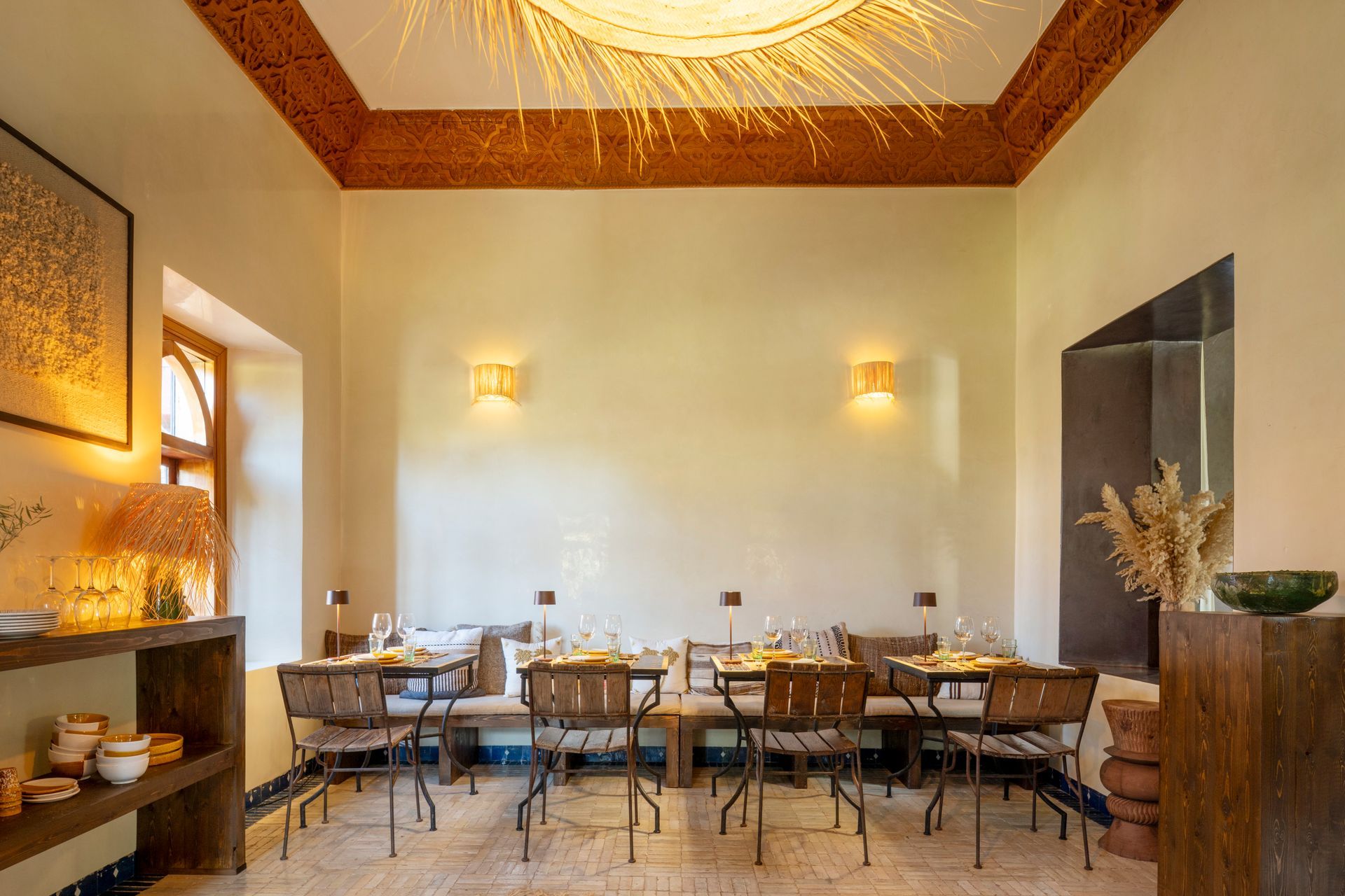 Warm dining room with wooden tables, chairs, wall sconces, and a high decorative ceiling