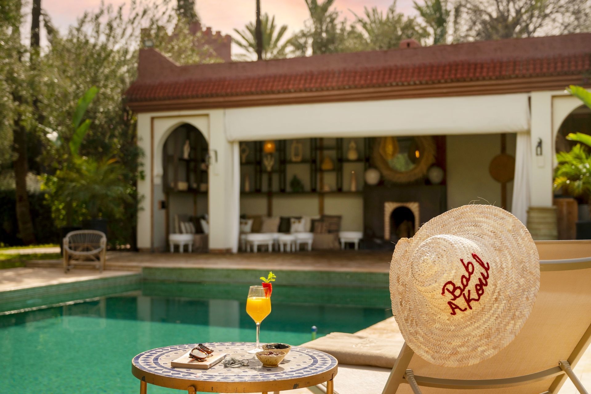 Poolside patio with a lounge chair, cocktail, and thatched beach ball by a villa
