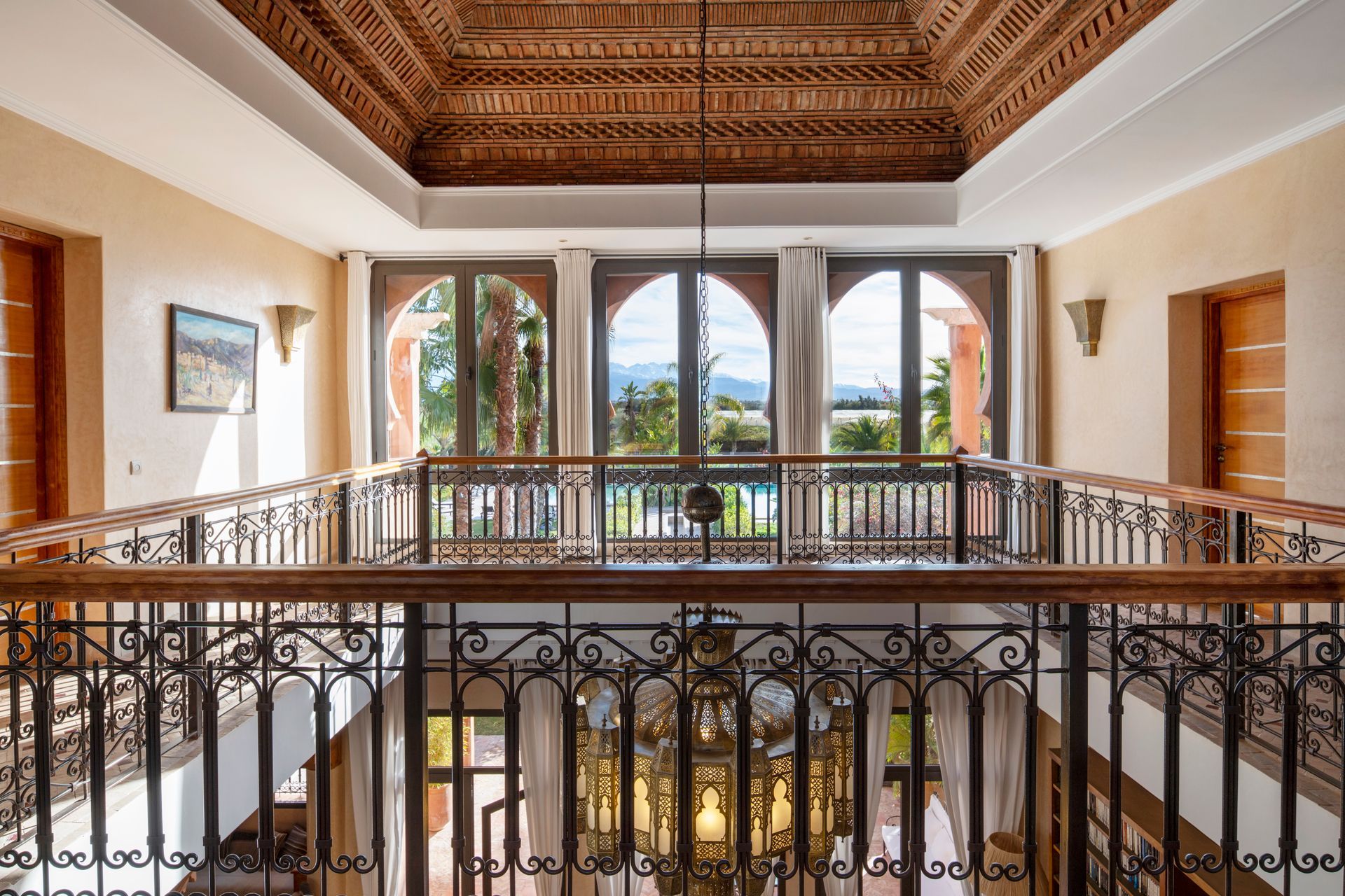 Elegant interior balcony with ornate iron railing, arched windows, and carved wood ceiling overlooking a courtyard