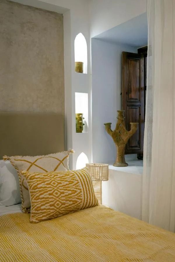 Cozy beige bedroom with yellow bedspread, opening to a sunny courtyard with blue lounge chairs