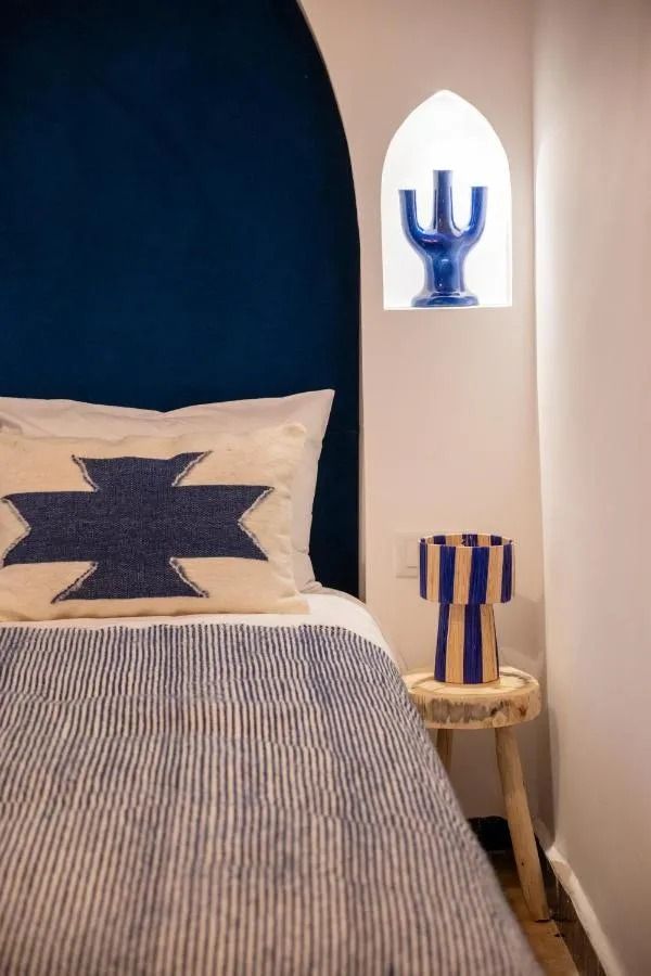 Blue-and-white bedroom corner with patterned bed, striped pillow, and a small chair under a lit wall niche