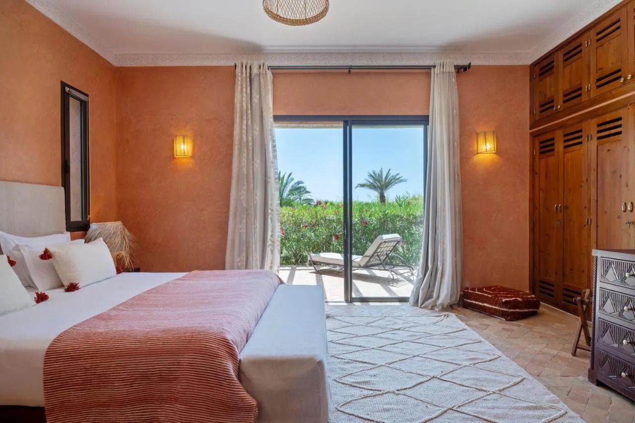 Bedroom with four-poster bed, patterned rug, and open glass doors to a patio and garden.