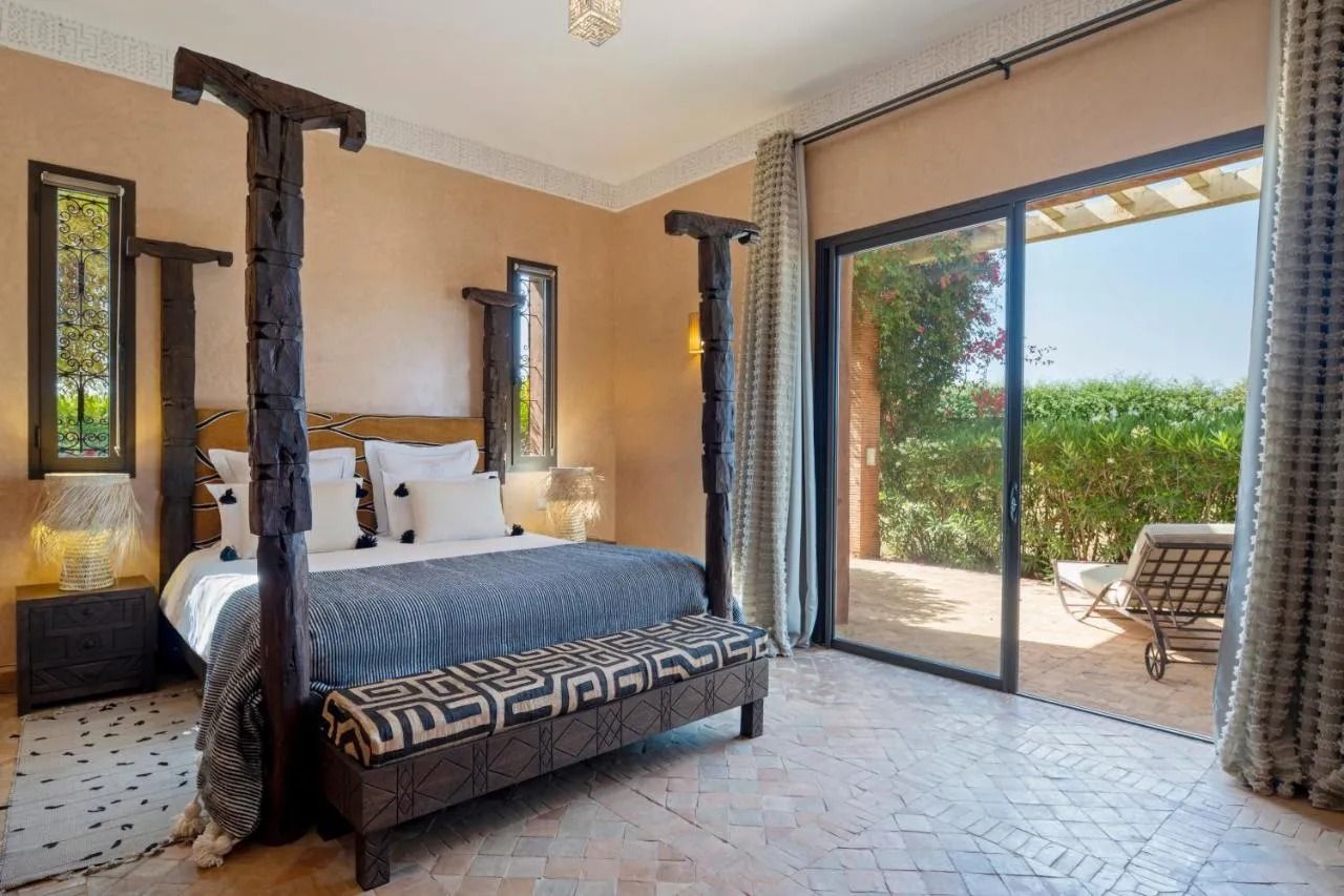 Luxury bedroom with four-poster bed and open sliding doors to a sunny patio and garden