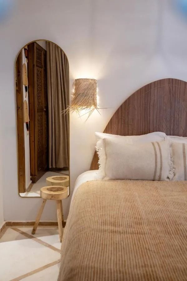 Cozy beige bedroom with woven decor, white bed, open wooden doors, and sunlit windows