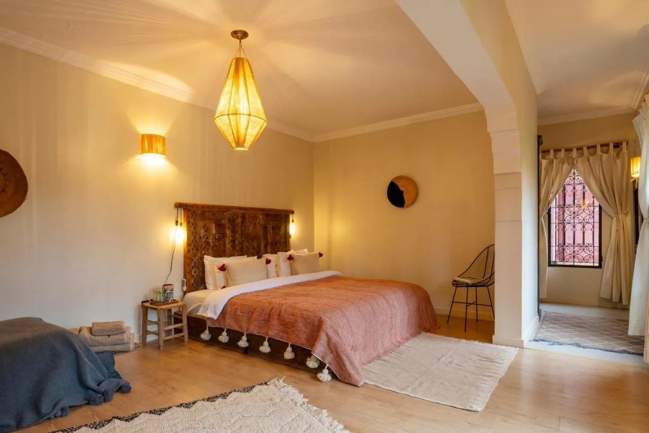 Cozy bedroom with pink bedspread, warm lighting, patterned wall art, and an archway to a sitting area
