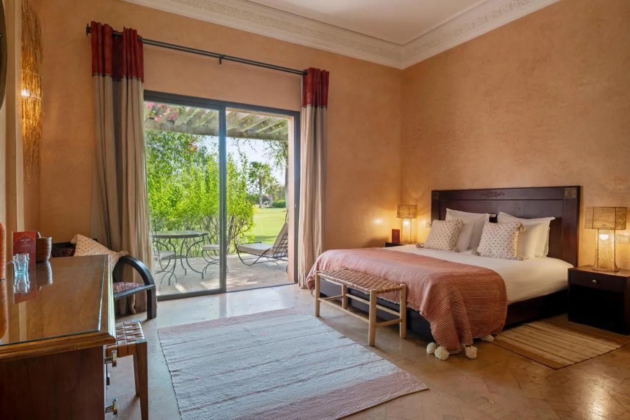 Bright bedroom with a bed, wooden dresser, and sliding glass door to a sunny patio and garden.