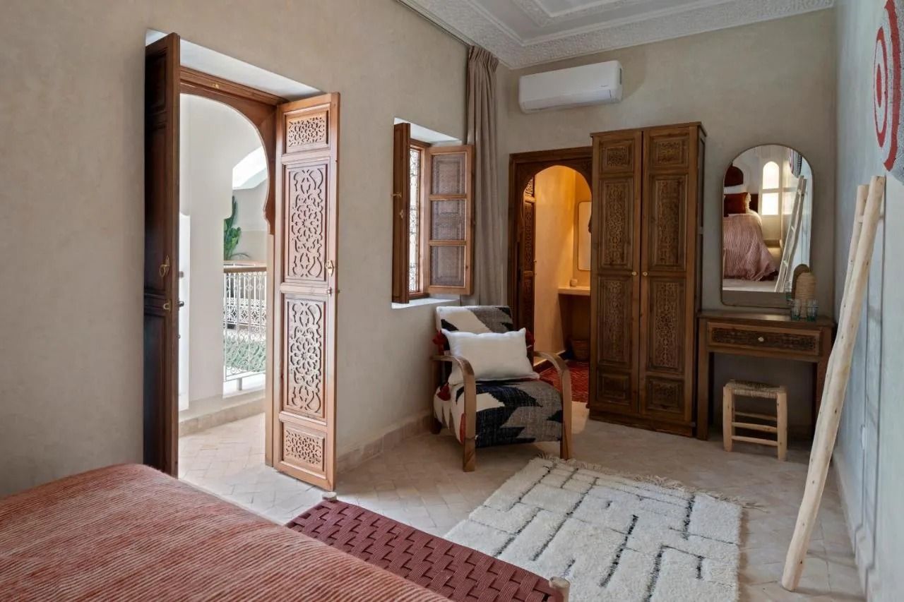 A cozy room with a bed, chair, wooden wardrobe, mirror, and open door to a balcony.