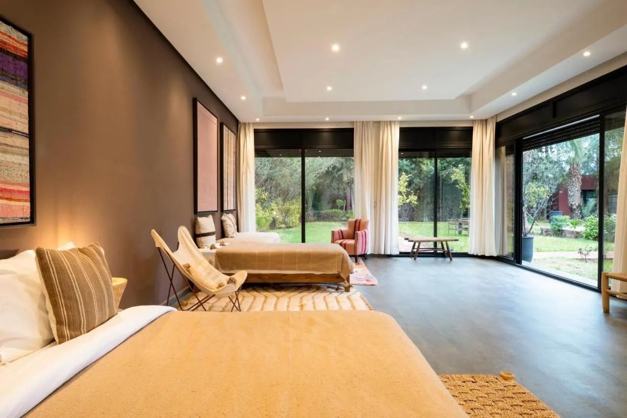 Modern bedroom with two beds, warm lighting, and large sliding doors opening to a garden view