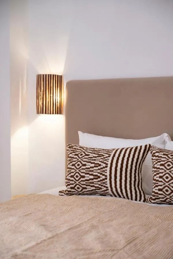 Cozy beige bedroom with a bed, woven pendant light, arched doorway, and a wall sconce on the right