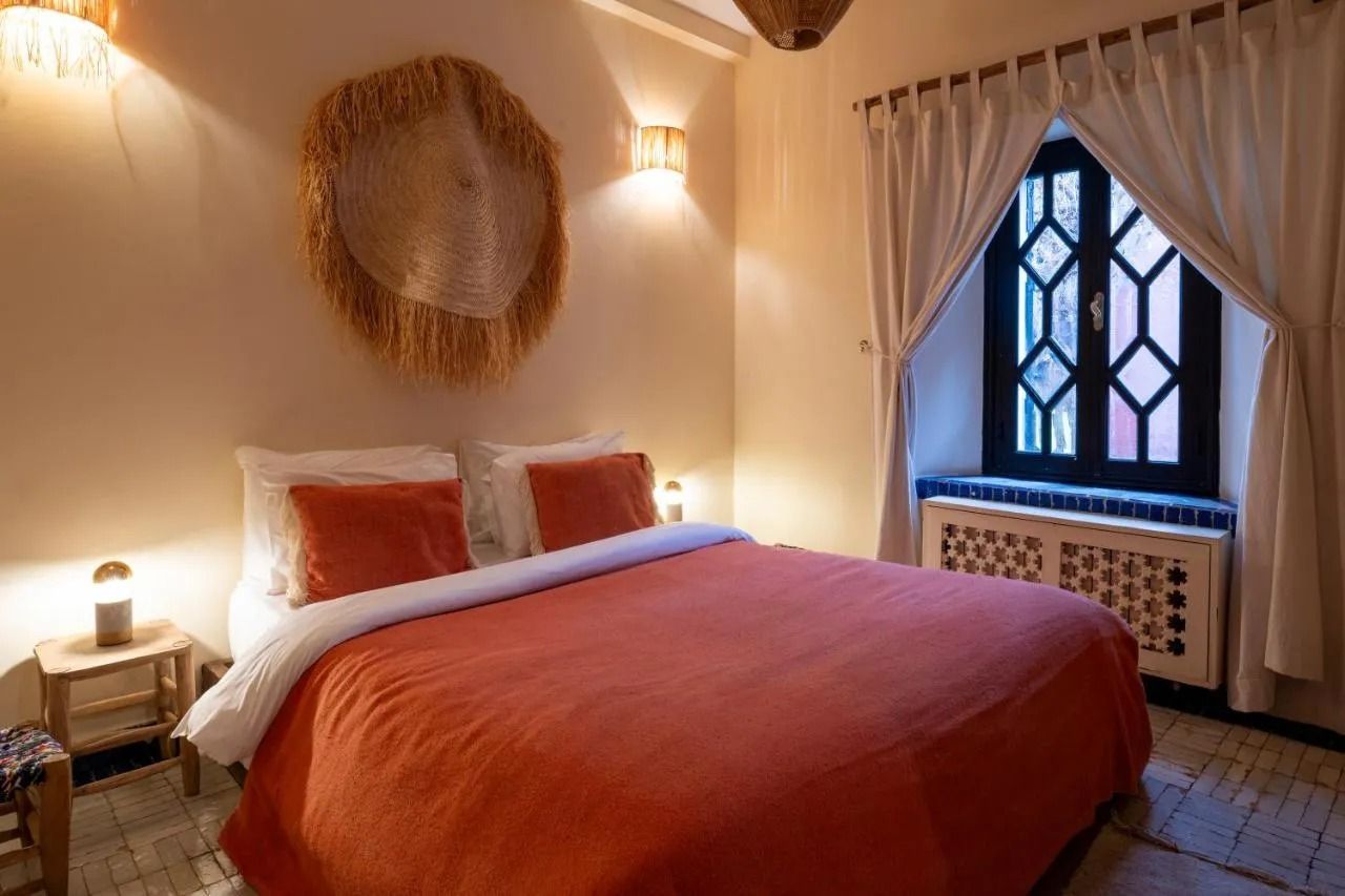 Cozy bedroom with a neatly made bed, warm lamps, and draped white curtains