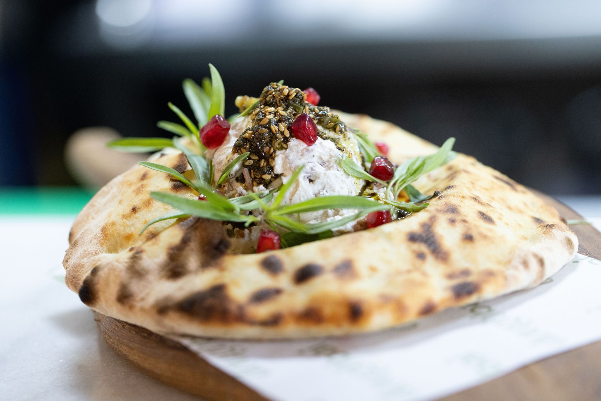 Flatbread topped with creamy salad, herbs, and pomegranate seeds on a wooden board