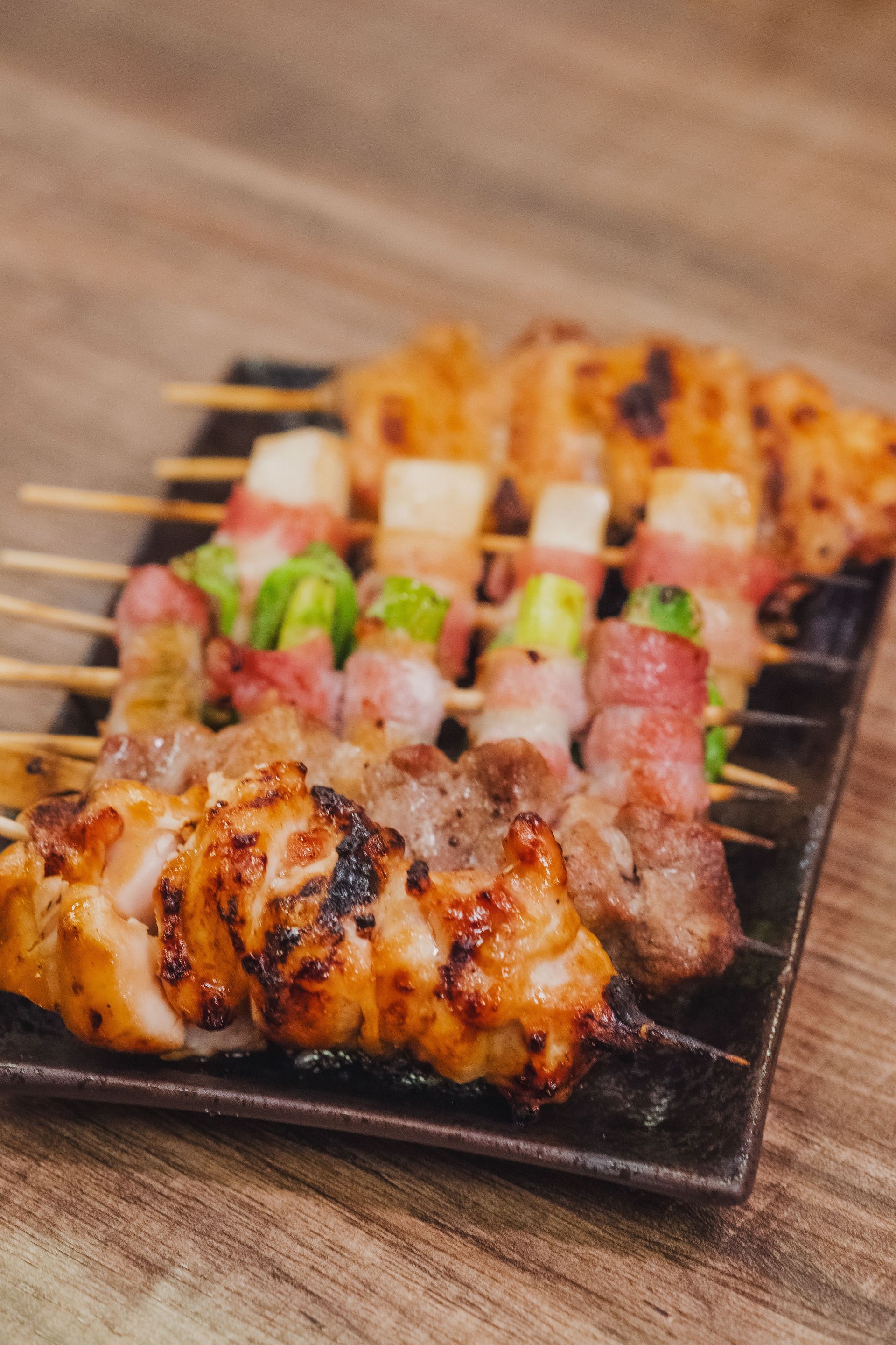 Grilled skewers of meat and vegetables on a small black plate on a wooden table