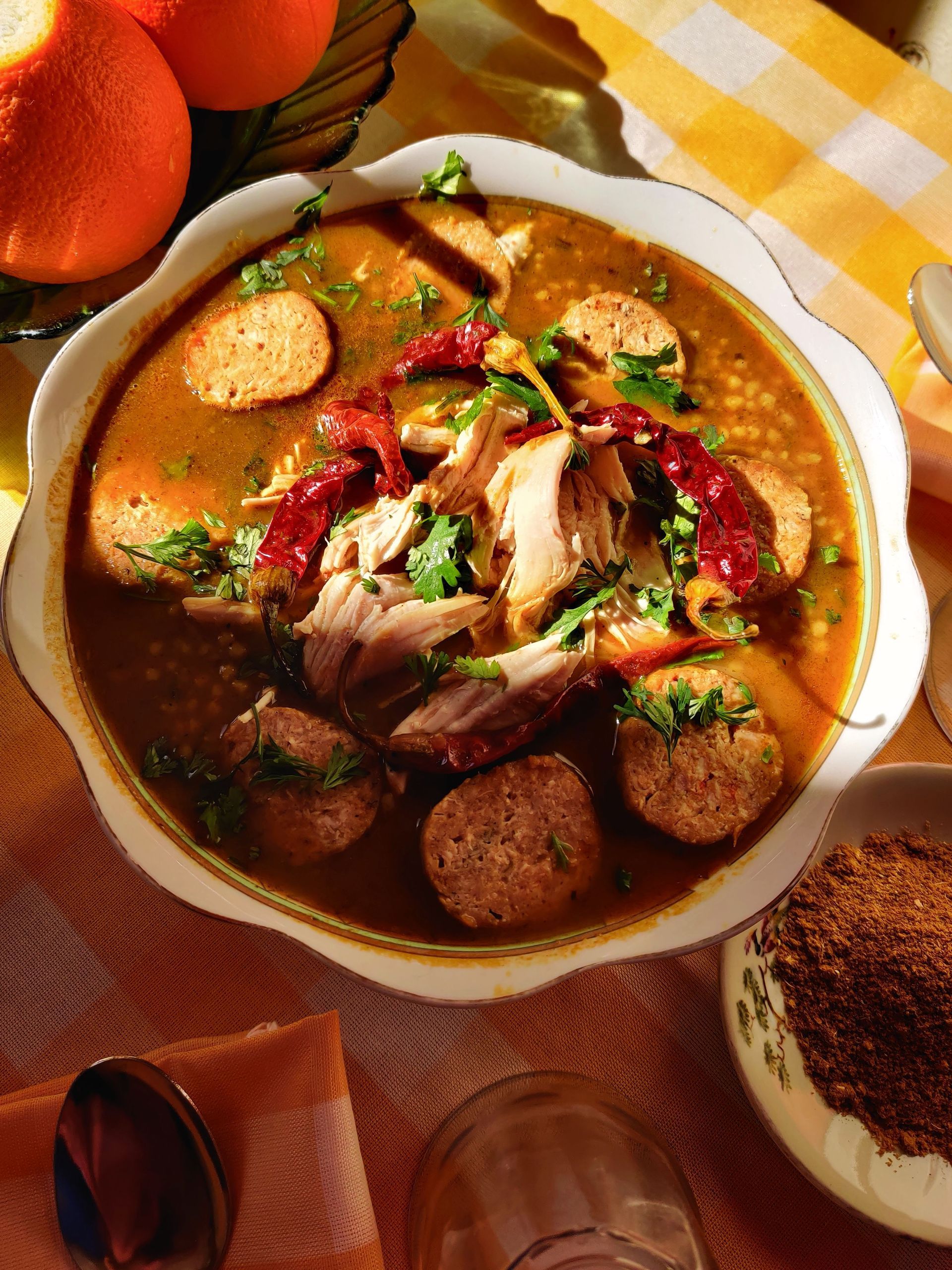 Overhead view of a bowl of rich stew with meat, herbs, and bread slices on a checkered tablecloth