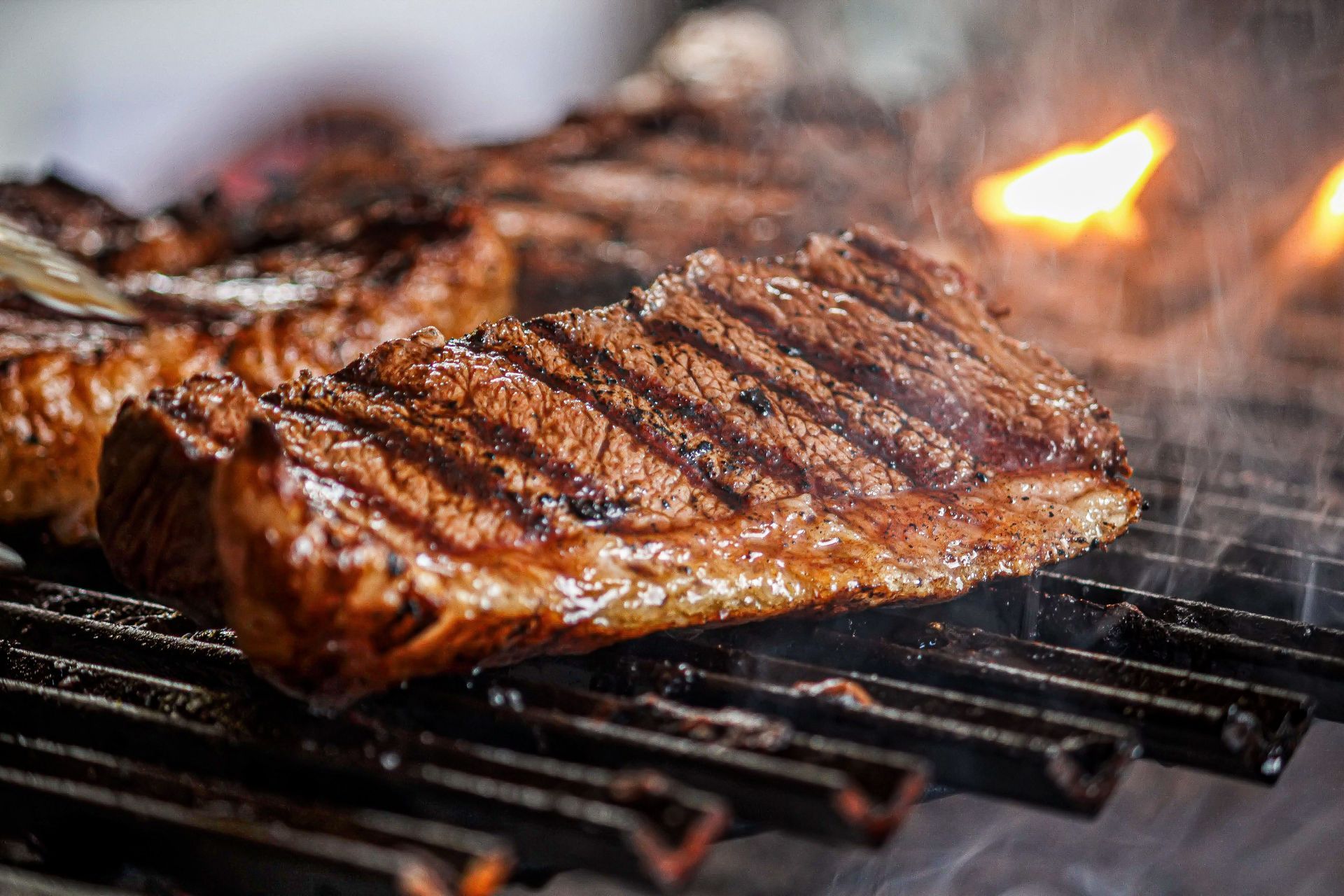 Grilled steak sizzling on a barbecue grate with visible flames and smoke