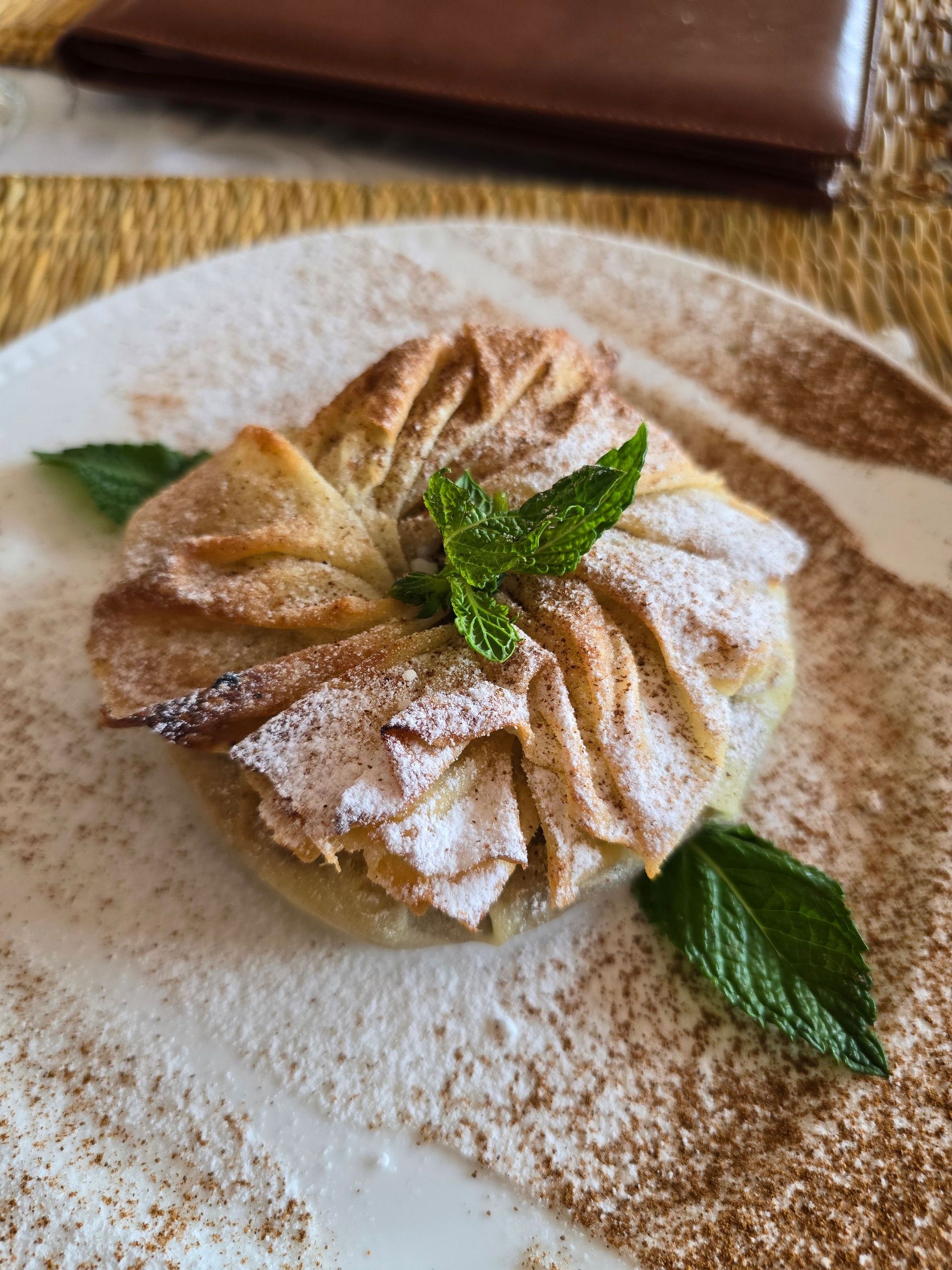 Powdered pastry dessert on a plate with mint garnish and cinnamon dusting
